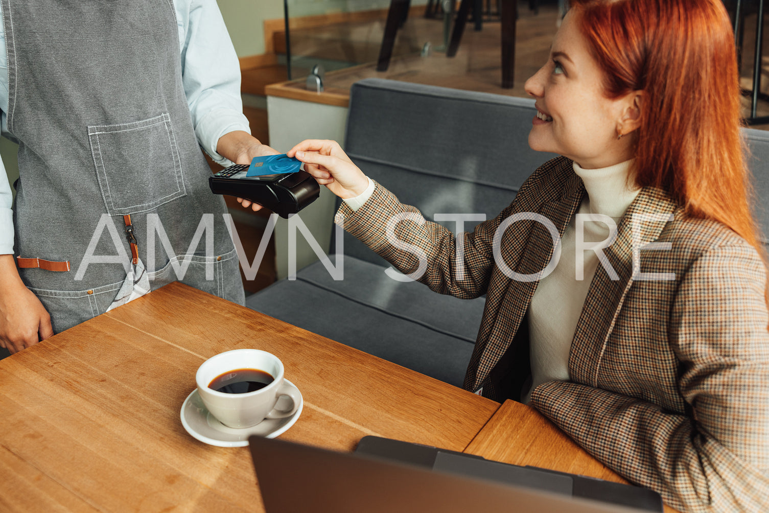 Woman paying by credit card with NFC in a coffeeshop. Female with ginger hair sitting at the table paying her bill.