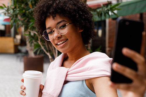 Young blogger taking selfie on her mobile phone, holding a coffee to go