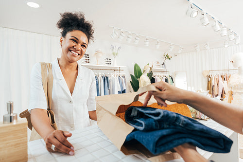 Unrecognizable saleswoman helping customer with purchase. Store owner packing the clothes in a paper bag.