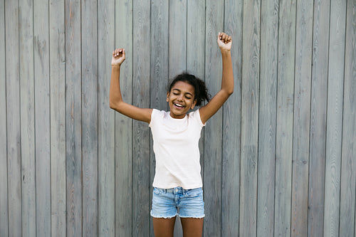 Happy girl standing at wall with raised hands