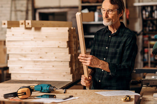 Senior carpenter wearing glasses holding a wood plank