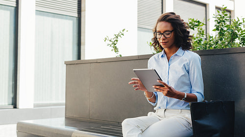 Woman sitting at office building and reading from digital tablet