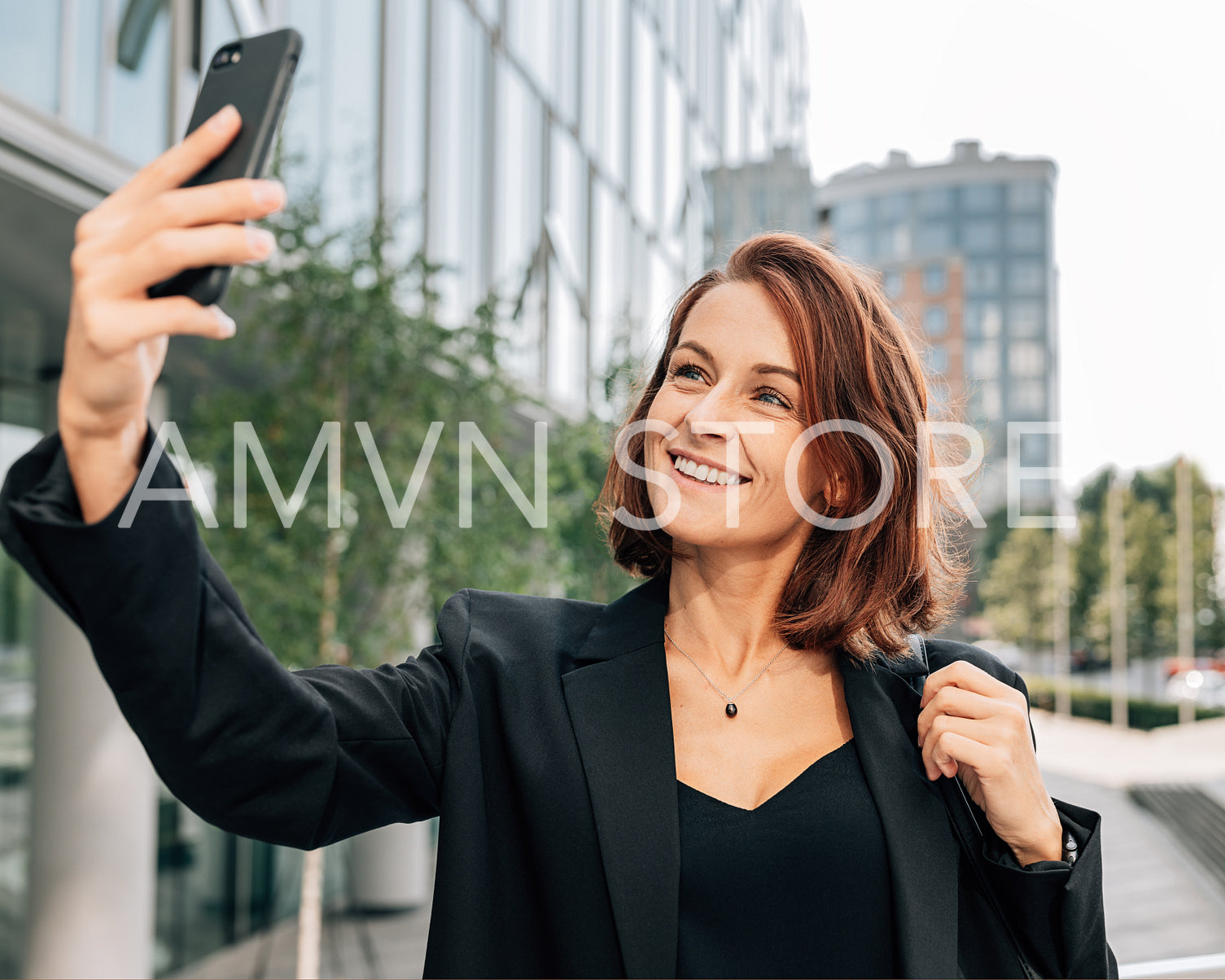 Smiling middle-aged businesswoman with ginger hair taking a selfie outdoors on her smartphone