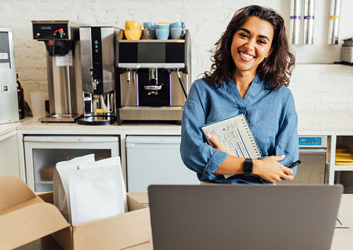 Portrait of a happy female coffee shop owner. Businesswoman holding a notebook in the cafe and looking at camera.