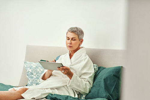 Mature woman relaxing at home. Senior female making online order while lying on a bed.