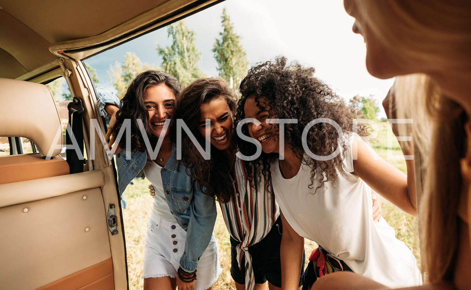 Group of friends on road trip laughing at van. Young people standing together and having fun at minivan door.