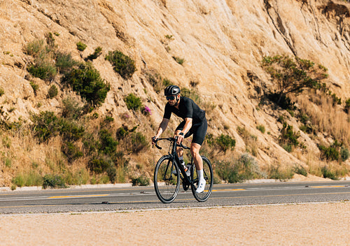 Young male in black sportswear riding a bicycle on an empty road a mountain