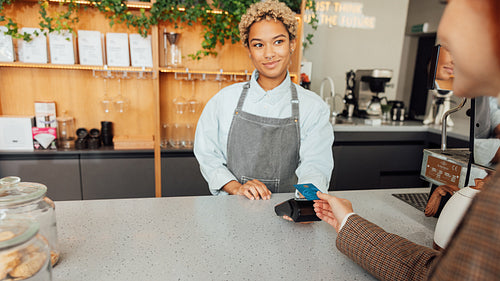 Woman bartender receives payment from a customer. Barista in apron holding pos terminal while customer paying buy card.