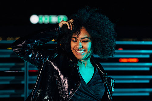 Smiling woman posing under colored light at night and looking down