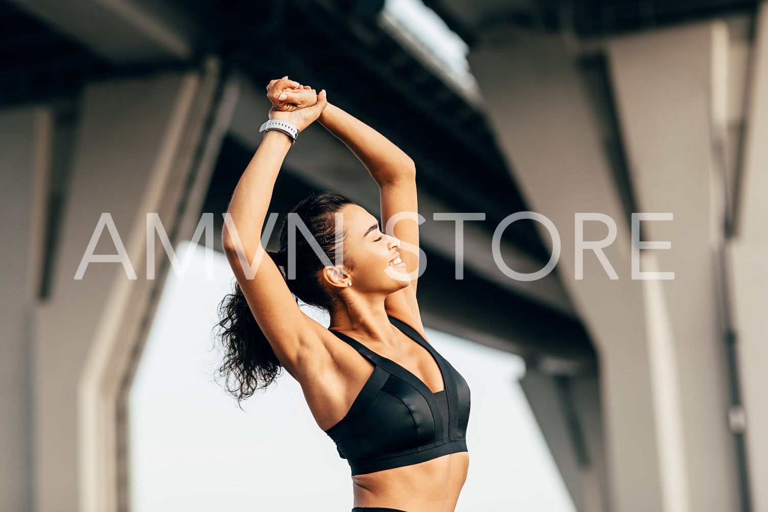 Happy athlete stretching her arms against under a highway at evening	