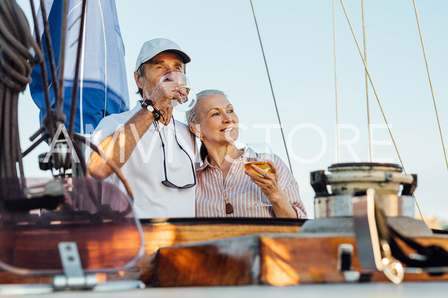 Portrait of senior couple standing on a private sailboat and drinking wine. Woman and man with bocals of wine on yacht enjoying trip.	