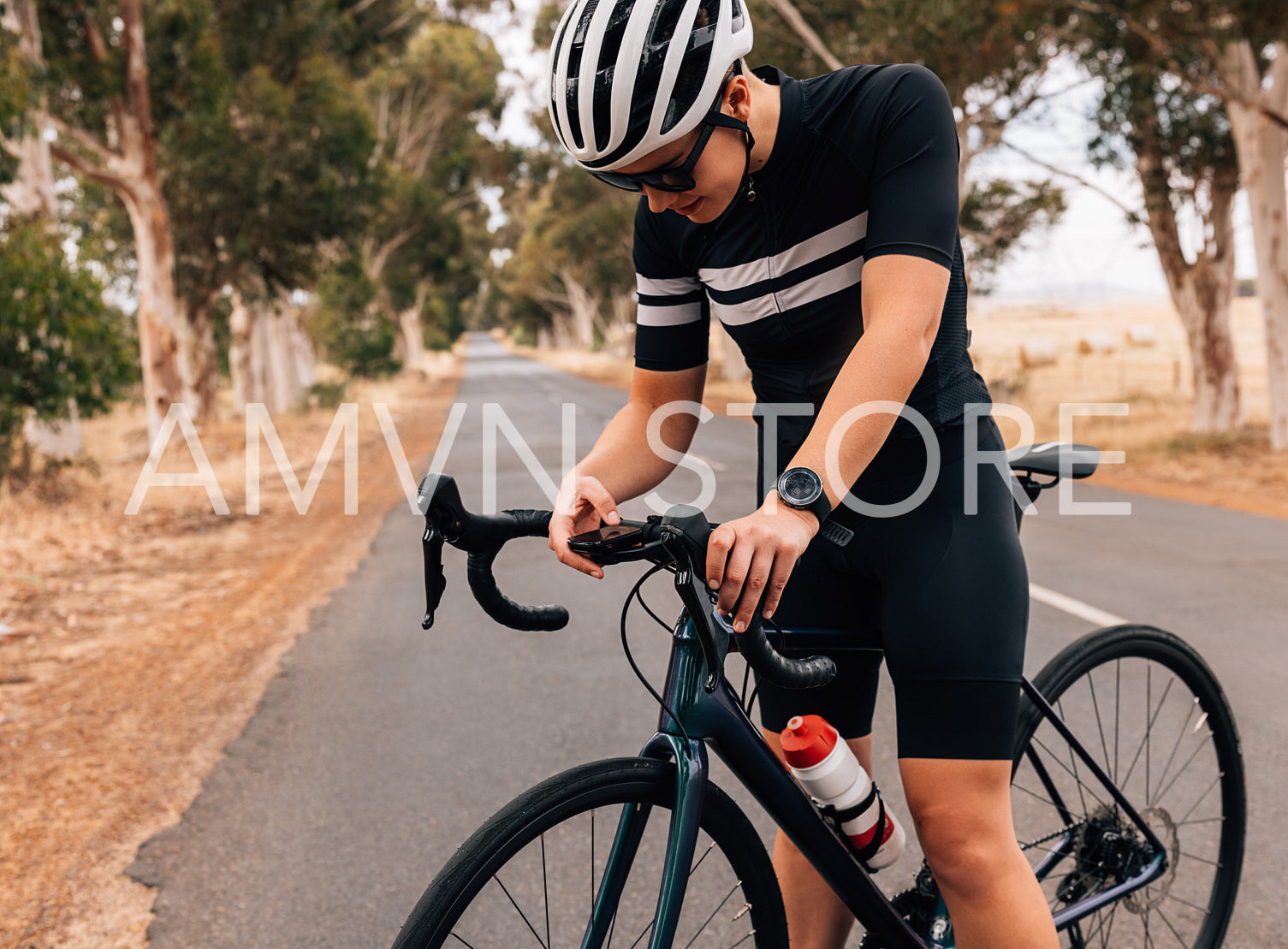 Professional woman cyclist checking on board computer on her road bike on empty road