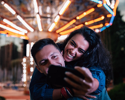 Young happy couple taking selfie while having fun at night in an amusement park