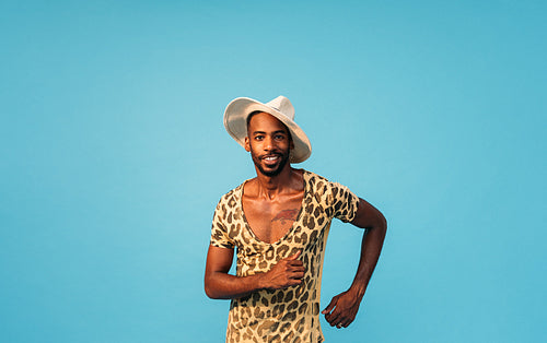 Stylish man in straw hat dancing in studio and looking at camera against blue background