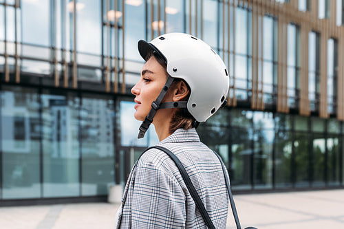 Side view of a young businesswoman wearing helmet standing outdoors near office building