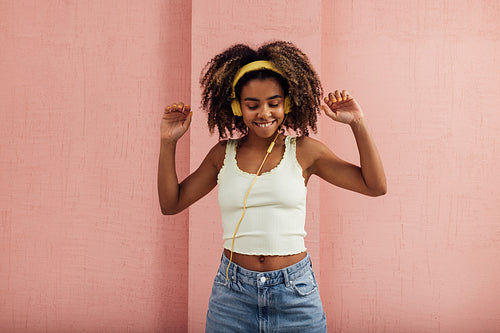 Cheerful woman in yellow headphones enjoying music raising hands