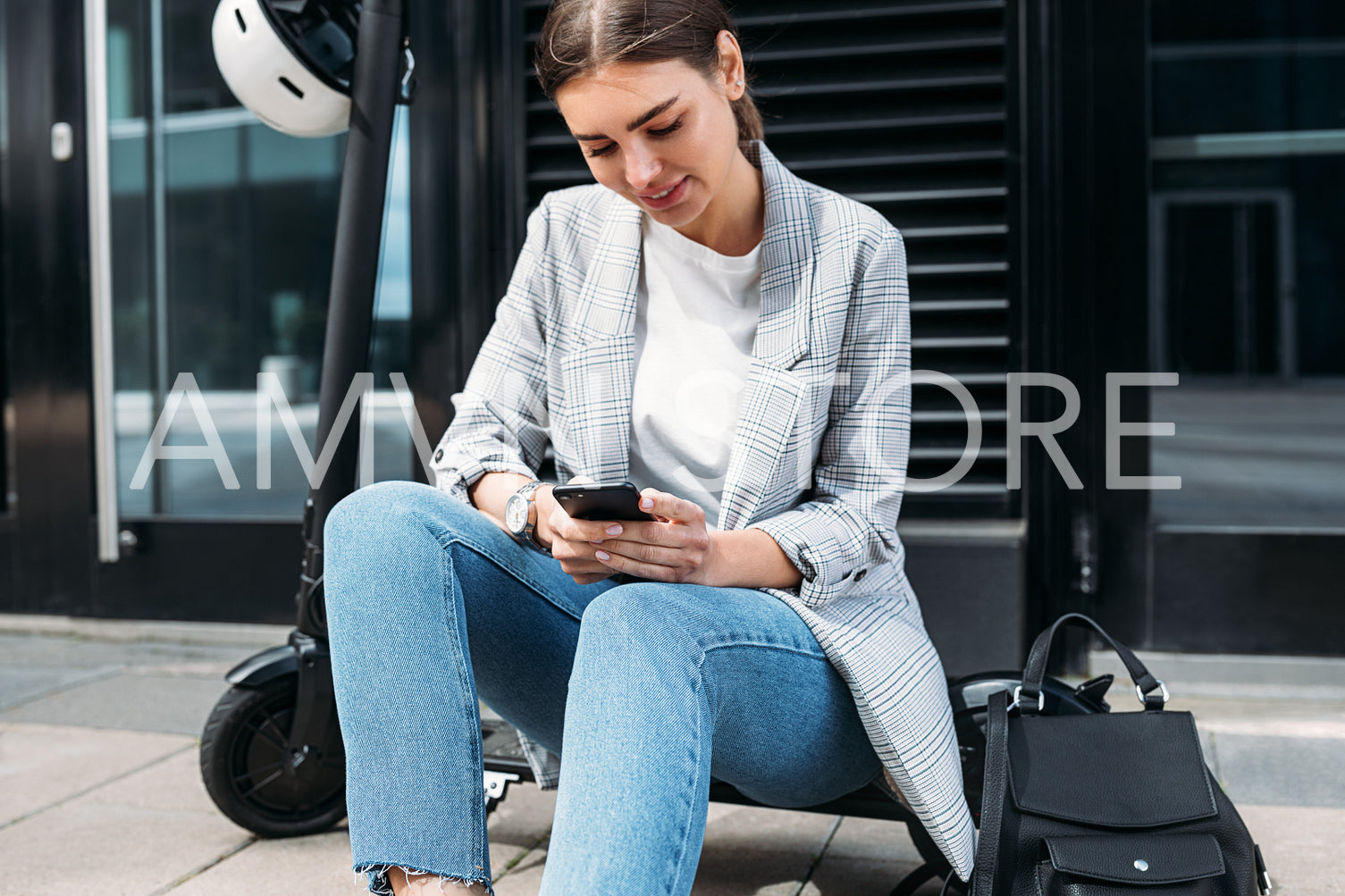 Businesswoman typing on a cell phone while sitting on electric push scooter at building