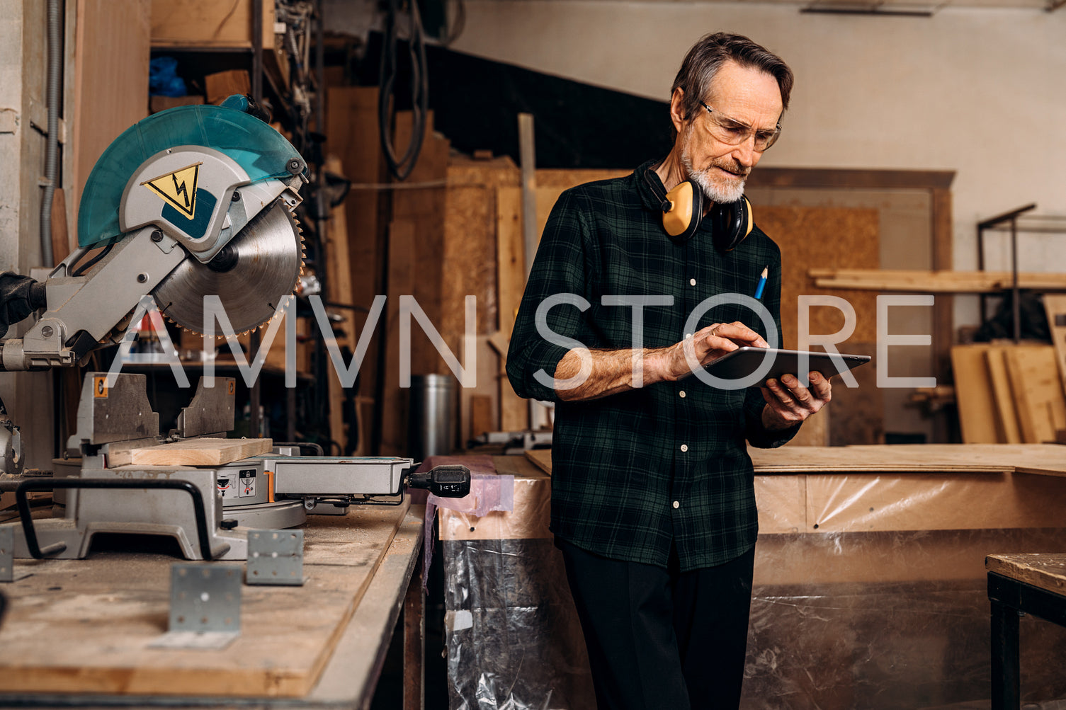 Mature carpenter holds a digital tablet. Male worker standing at workbench in carpentry.	