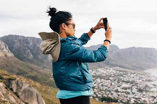 Side view of a woman in sports clothes holding a smartphone in vertical position shooting content for social media