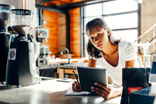 Cafe owner leaning on counter making notes in cafe