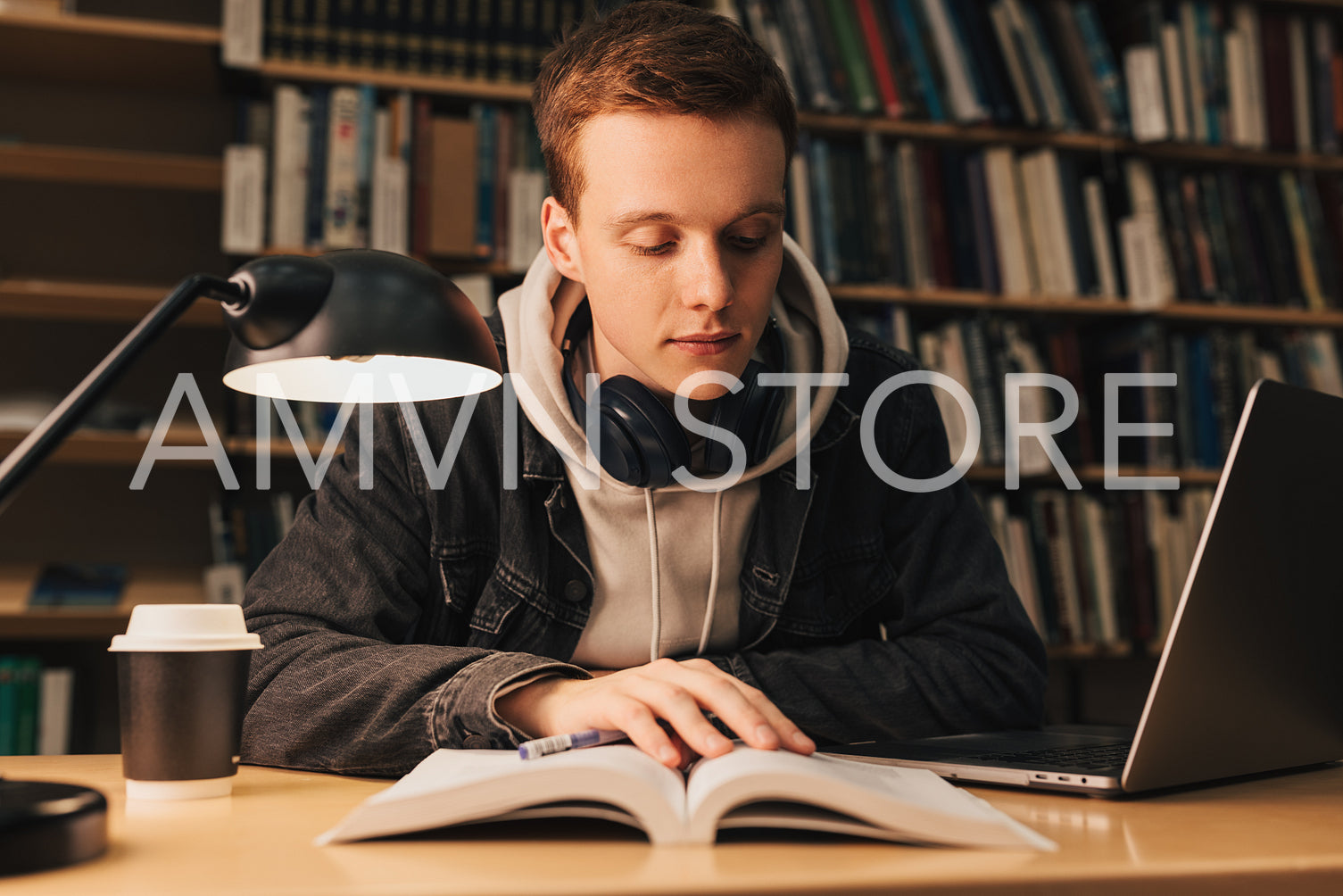 Handsome guy with ginger hair reading book late evening in library sitting at table