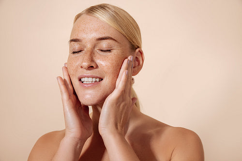 Studio shot of a young blonde woman touching her face with close