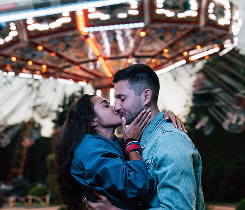 Side view of a young couple kissing during festival against carousel