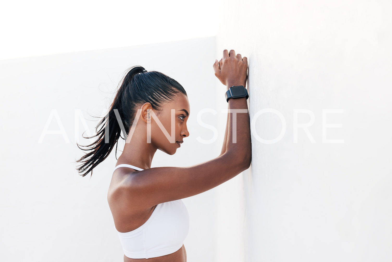 Slim female leaning on a white wall during fitness training. Woman relaxing at a wall during workout.