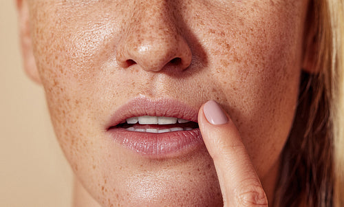 Close-up of unrecognizable woman with freckled skin touching lips with finger