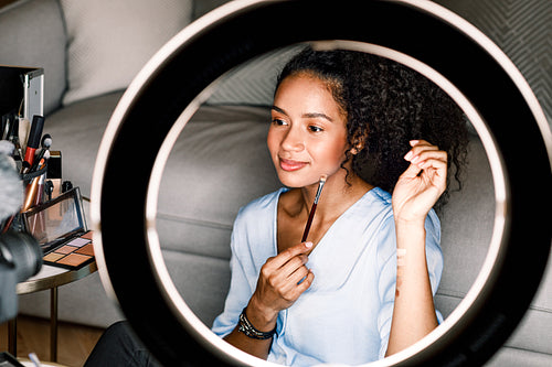 Makeup artist recording video from home. Woman applying cosmetics sitting in front of ring light.