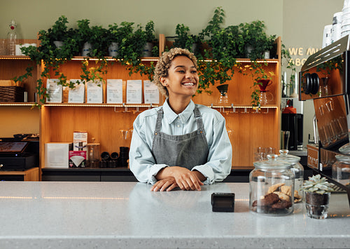 Young happy barista at the counter. Woman working as a barista standing at a cafe.