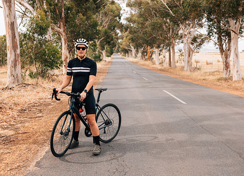 Professional female cyclist taking a break on a long empty countryside road