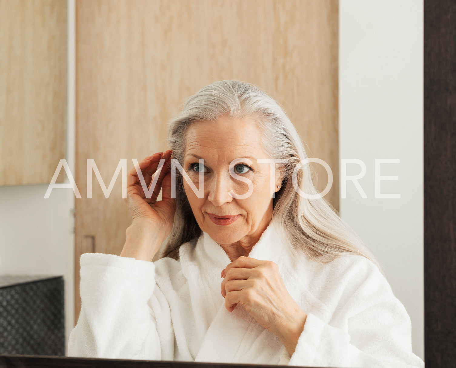 Senior woman adjusting and examines her hair in bathroom mirror in morning