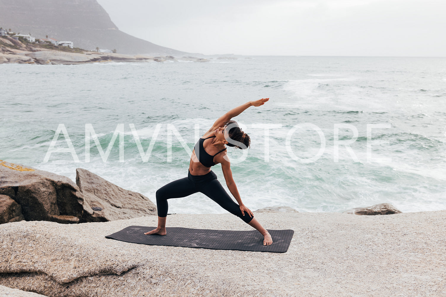 Young woman practicing Reverse Warrior pose by ocean at sunset. Female flexing her body on mat outdoors.