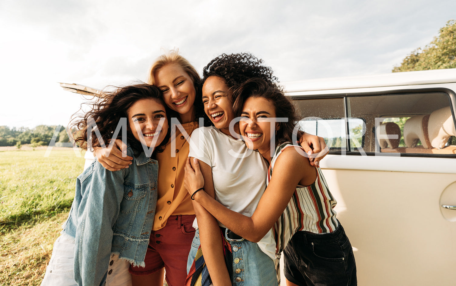 Four happy female friends laughing together standing in front of a van. Women enjoying summer road trip.