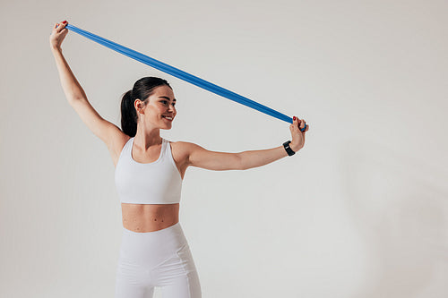 Smiling woman in white fitness attire warming up hands with resistance band