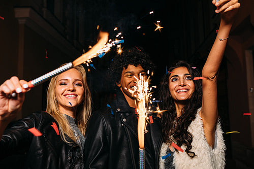 Young people having fun with sparklers outdoors, walking on city street