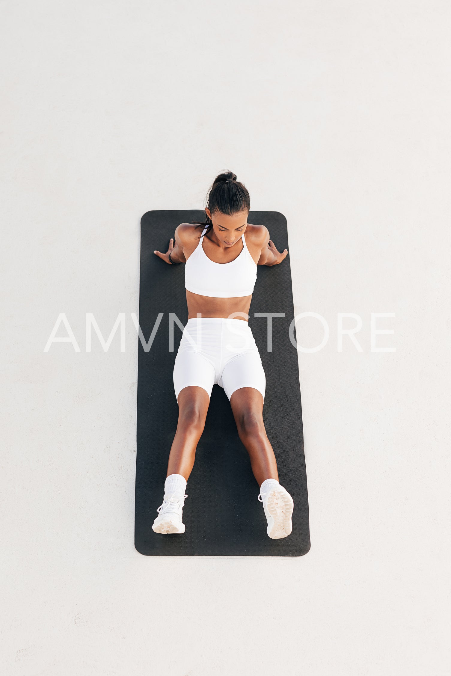 Shot from above of a young sportswoman relaxing on a mat. Female in white fitness wear taking a break.