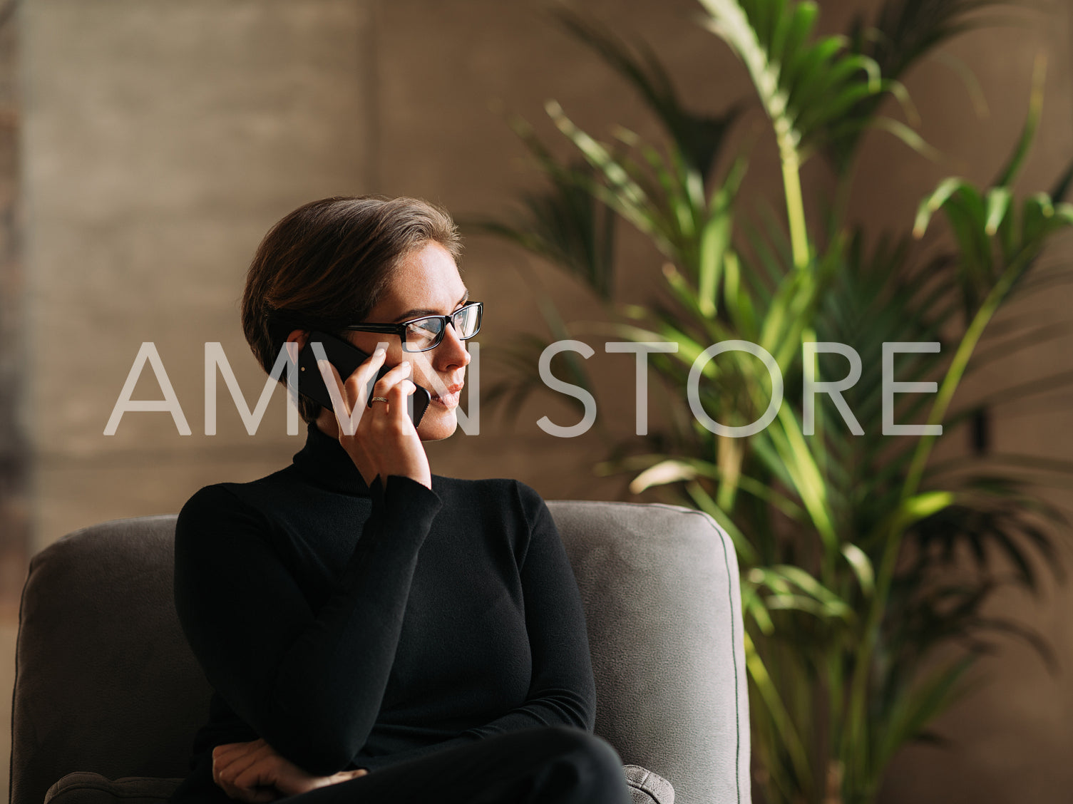 Serious and confident businesswoman in black formal wear looking away while sitting and talking on mobile phone