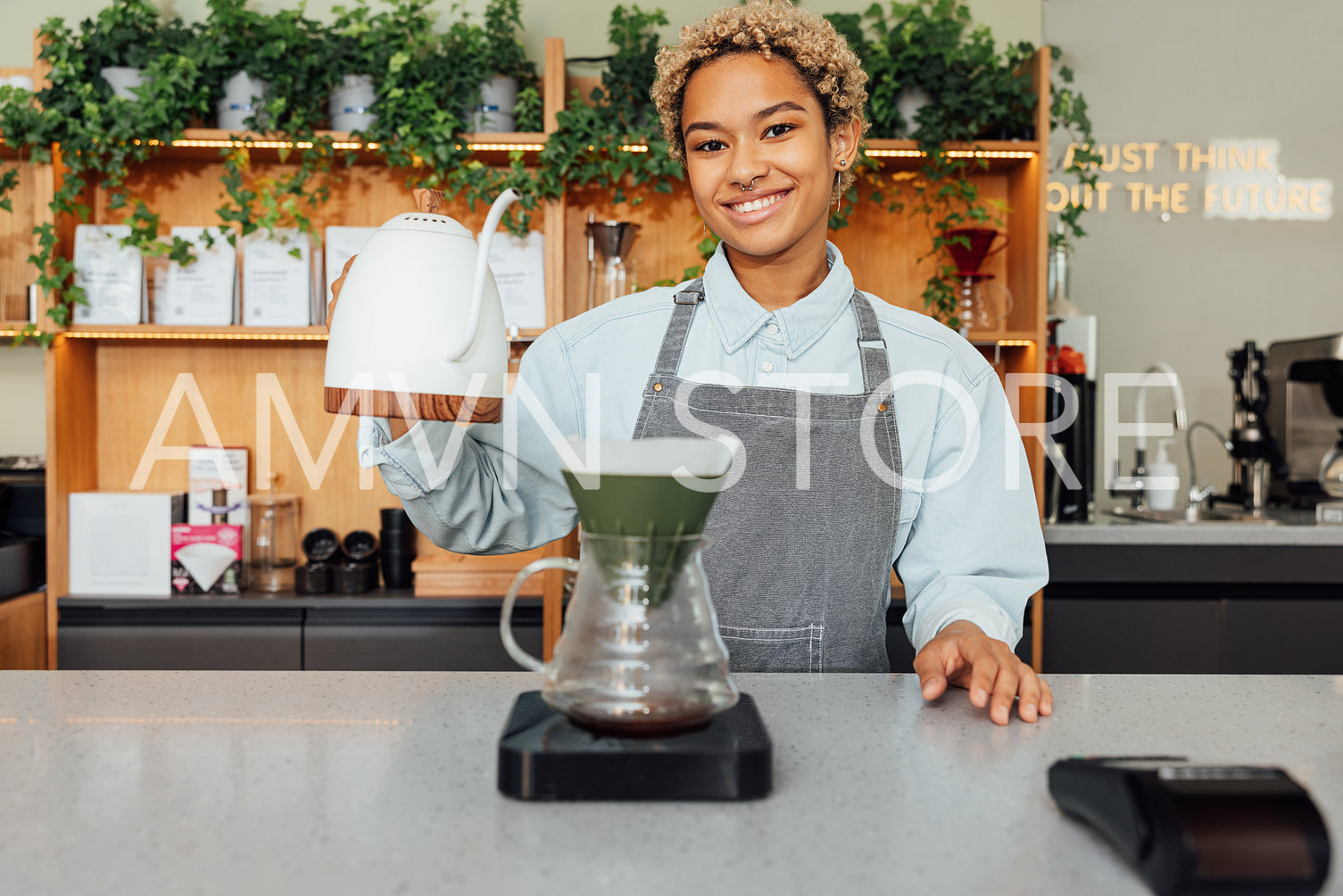 Smiling female barista holding a kettle while standing at a counter in coffee shop