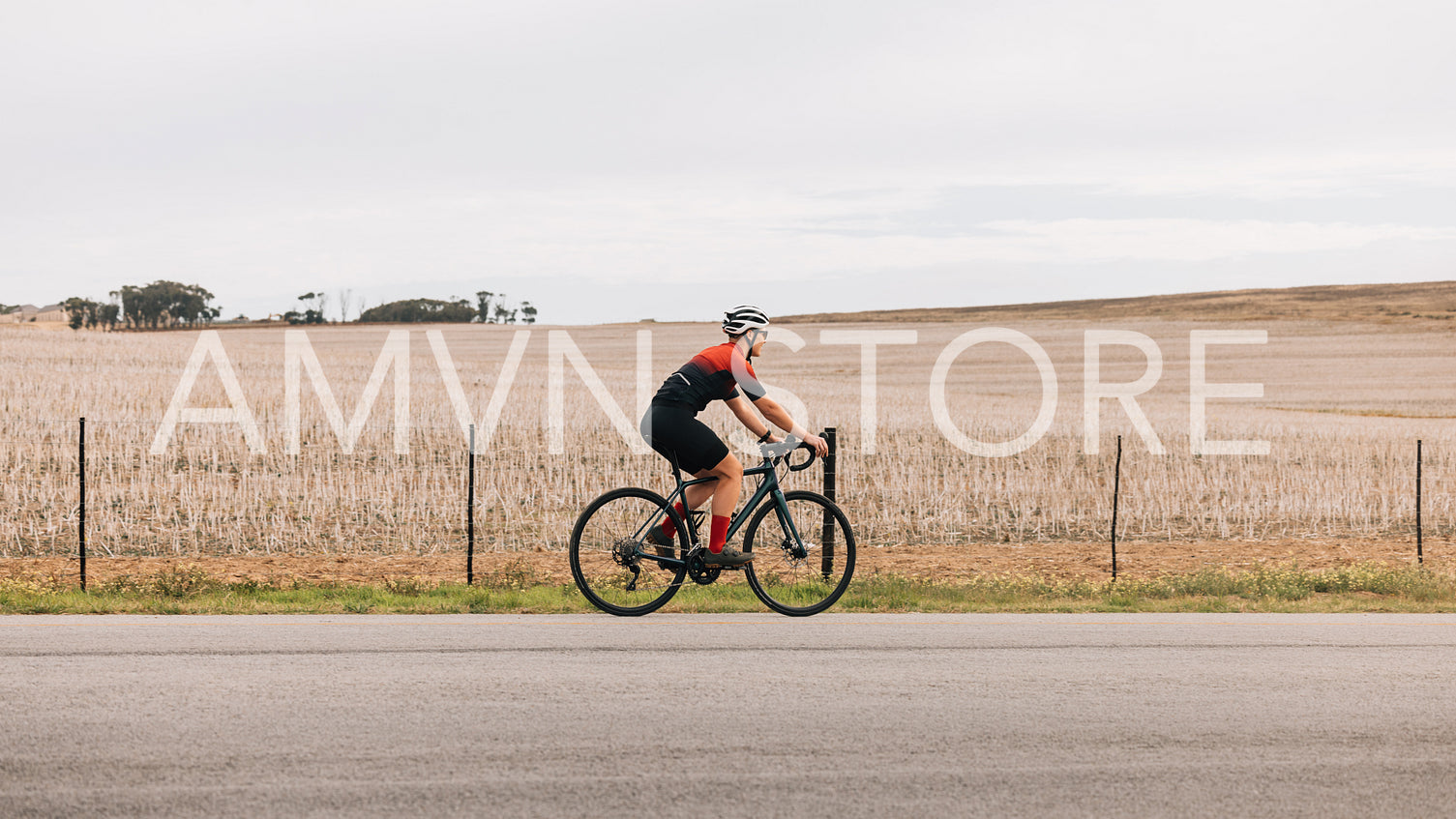 Woman cyclist exercising outdoors on road bike against agriculture field