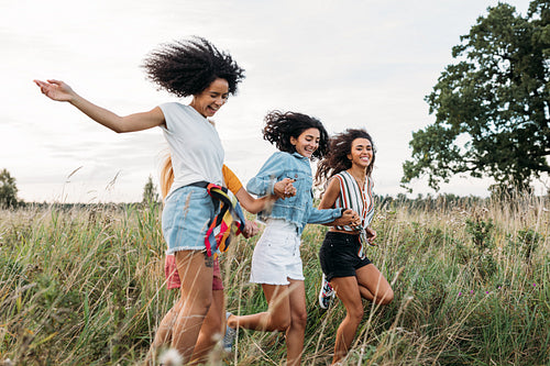 Four women holding hands running on field. Laughing friends having fun outdoors in summer.