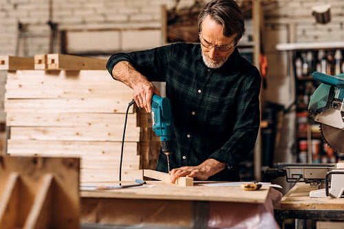 Carpenter using electric drill. Senior man making a hole in a wooden board.