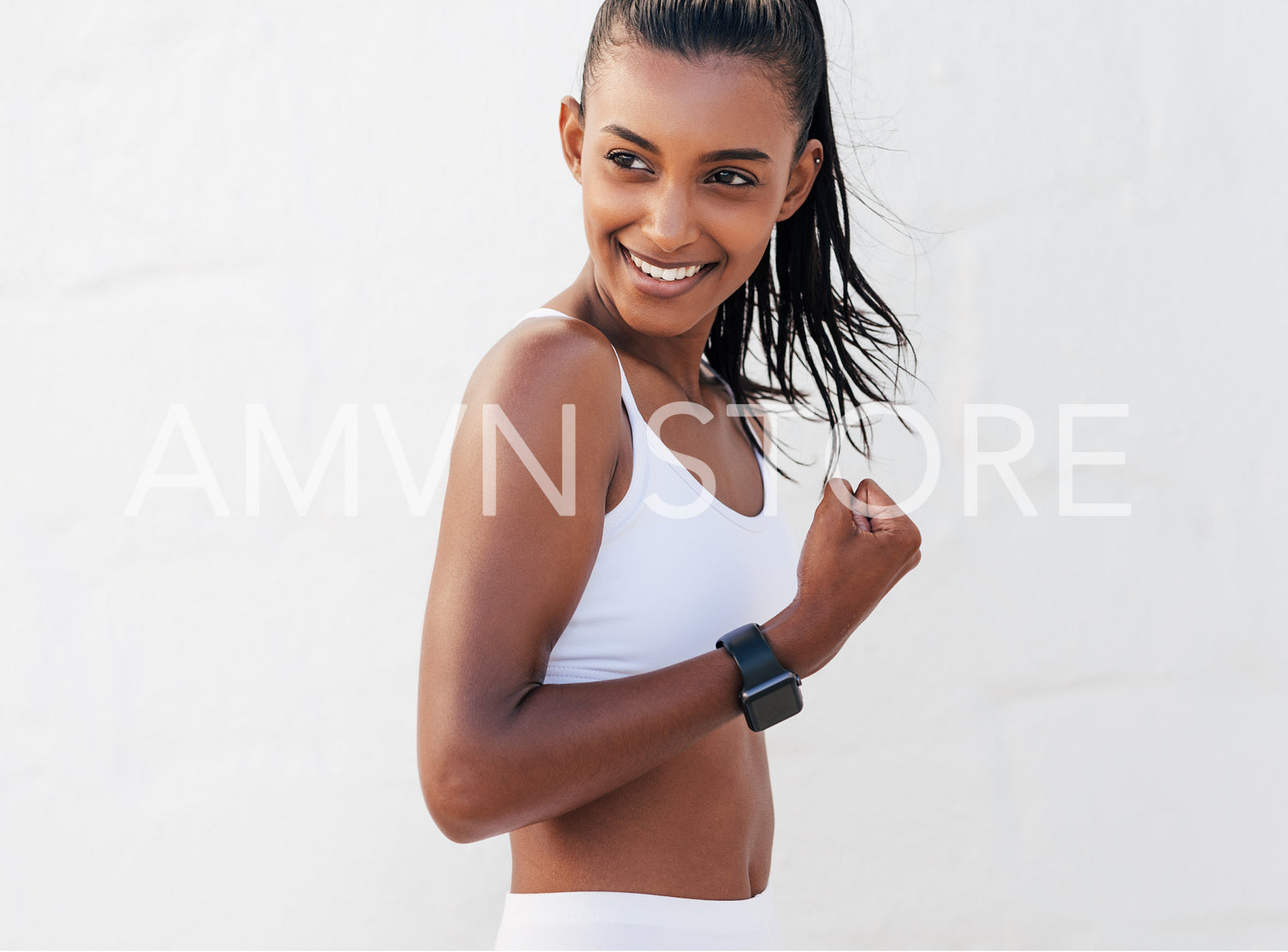 Cheerful woman flexing her hand showing muscles. Smiling female in white fitness attire strains the biceps.