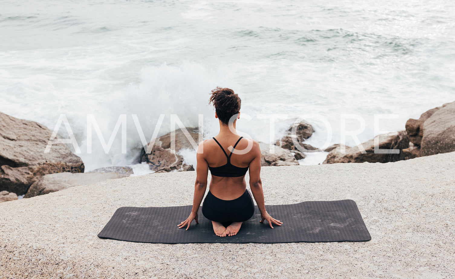 Back view of fit woman sitting by ocean and looking at waves after workout