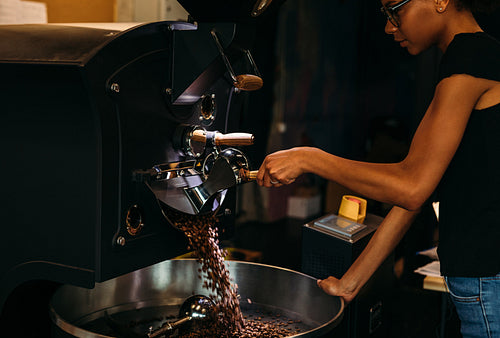 Young barista opening a coffee roaster, beans falling out into the cooling pan