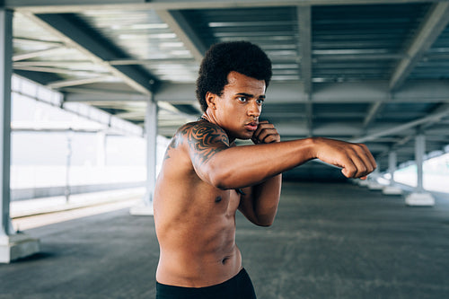 Young bare chested kickboxer doing shadow boxing, practicing his punches outdoors