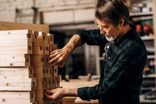 Senior carpenter using measuring tape on a bunch of wooden parts