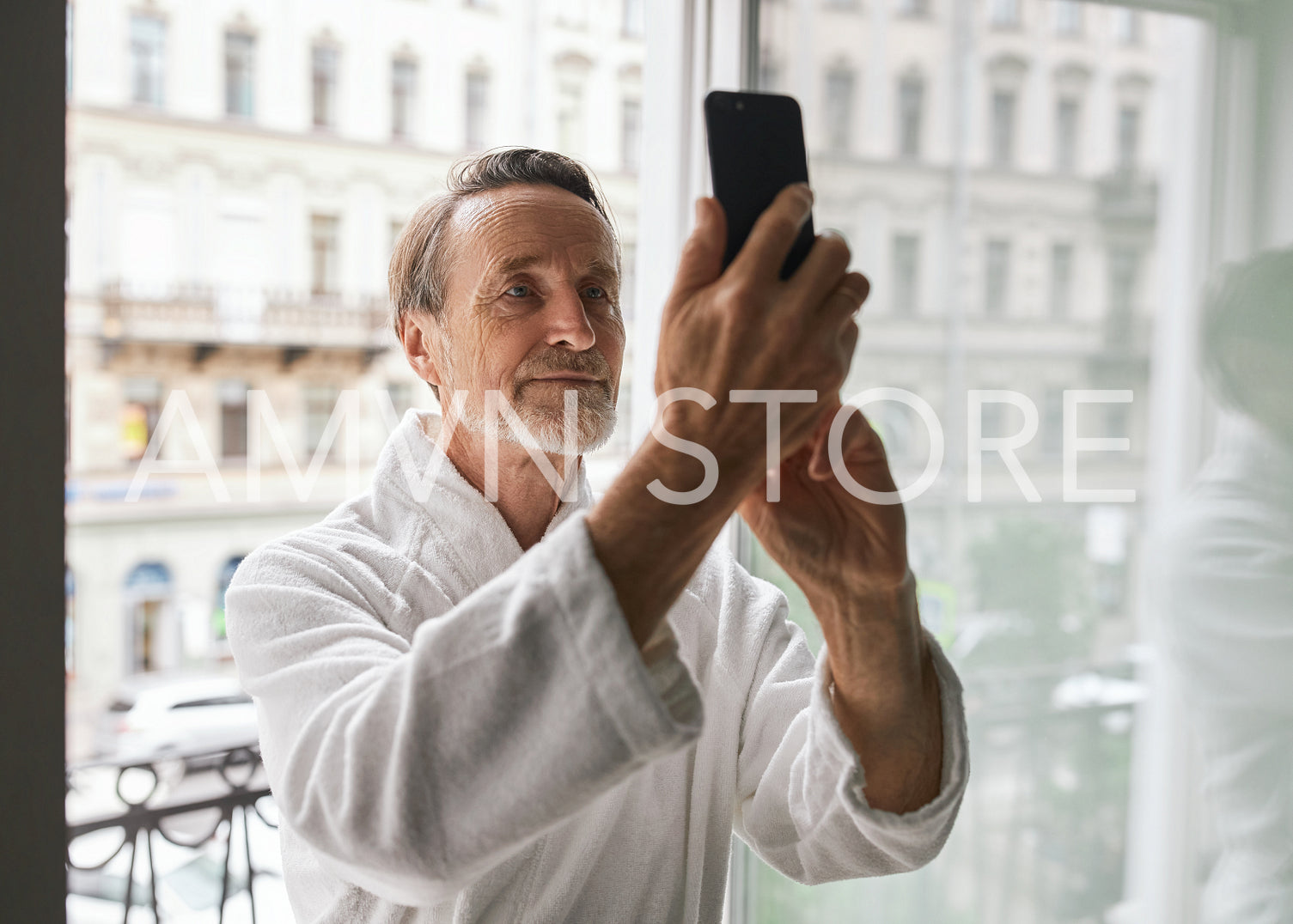 Senior man wearing bathrobe standing on balcony of a hotel room and taking a selfie	