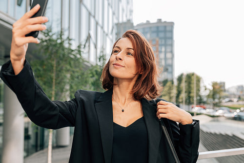 Middle-aged businesswoman with ginger hair taking a selfie while standing outdoors